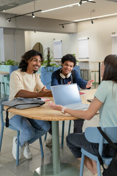 Diverse coworkers discussing project in modern office around wooden table with laptop and backpack