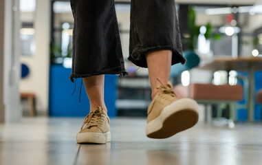 Tan platform sneakers stepping across smooth tiled floor in lobby, with blurred seating and plants