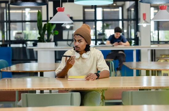 African American men wearing tan beanie and headphones sitting in study lounge recording on phone