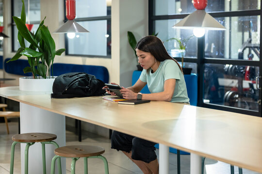 African American woman in twenties sitting at coworking table using tablet backpack notebook pen