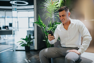 A professional man smiles while using a smartphone in a modern office.