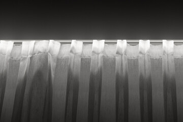 A grayscale image of translucent white curtains hanging along a window, glowing softly from behind. The calm, minimal mood suits home decor, interior design, and lifestyle visuals