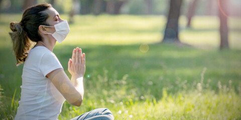 Lifestyle background. Side view of a woman wearing a mask meditating on green grass in a mental health care concept