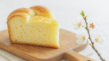 Slice of soft homemade Easter bread on wooden cutting board with spring blossom branch on white background.