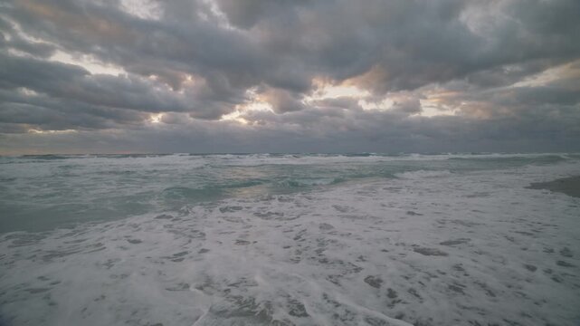 Ocean waves under dramatic overcast sky with light breaking through clouds