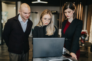 Three professionals review data on a laptop in a modern office. A collaborative team examines information on a computer in a contemporary workspace.