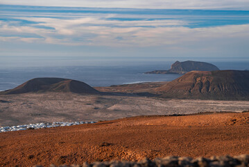Volcanic cones and lava fields descend to the Atlantic near Mirador del Rio, Lanzarote. La Graciosa and Montana Clara sit offshore, roads cross an arid plain.