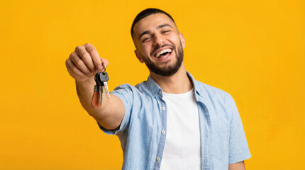Smiling man holding keys with a leather keychain celebrating his new home against a yellow background