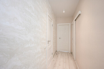 Fototapeta premium narrow, light-toned hallway with textured wallpaper, light wooden flooring, three white doors, recessed ceiling light, minimalist design, neutral palette.