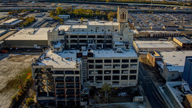 Aerial view of a decaying, multi-story industrial building with hollowed-out window frames and a prominent bell tower casts shadows on the snow-dusted grounds, Cincinnati, Ohio, United States.