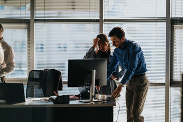 Two coworkers review details at a shared desk by a computer. An office scene shows focus and collaboration during a moment of discussion.