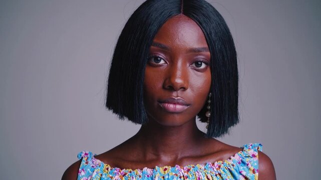 Gorgeous young african american woman with a stylish bob haircut and makeup looking directly at the camera in a studio with a grey background