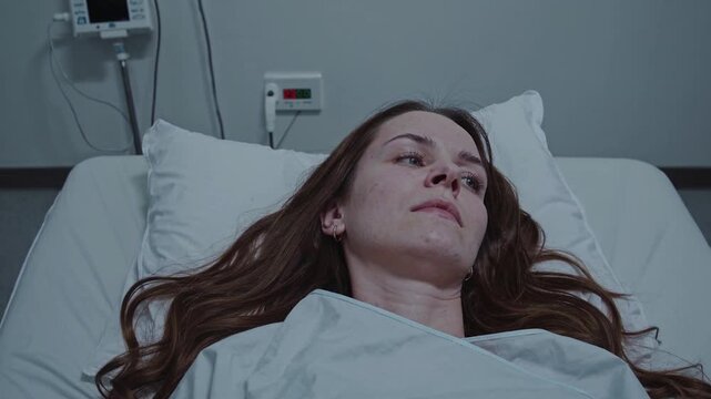 Sick young woman with long hair lying in a hospital bed. A thoughtful patient recovering from illness or injury in a modern clinic ward