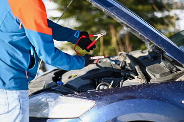 Fototapeta premium Person connecting jumper cables to a car battery under an open hood