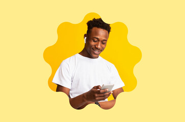 A young man smiles while looking at his smartphone. He wears wireless earbuds and stands against a bright yellow background. The scene captures a moment of enjoyment and technology use.