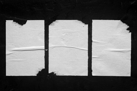 three white posters with folds on a black wall