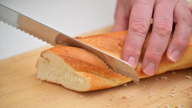 A person is cutting a loaf of bread with a knife on a wooden cutting board