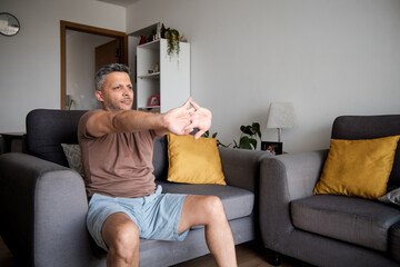 Mature Man Lifting Dumbbells and Exercising on Home Sofa