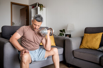 Mature Man Lifting Dumbbells and Exercising on Home Sofa
