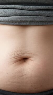 Vertical video: Lifting gray shirt, hands revealing abdomen in closeup to show navel and scar