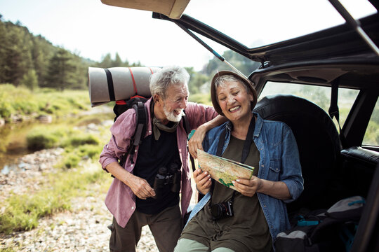 Smiling senior couple reading map by car in nature
