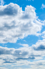 Fototapeta premium Blue sky background with white clouds lit by sunny light - natural vertical blue sky landscape