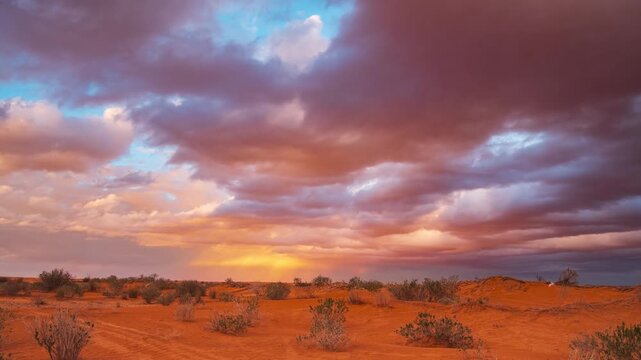 Timelapse: sunset over the desert near Ksar Ghilane, Tunisia, with red sand dunes and dramatic colorful clouds, conveying serenity and a timeless Sahara landscape ideal for travel and lifestyle themes