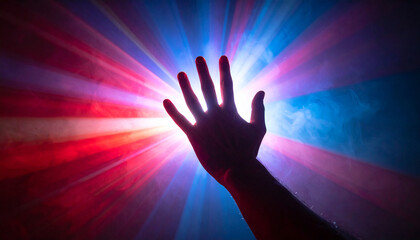 Silhouette of a hand reaching towards a bright burst of red and blue light rays and smoke