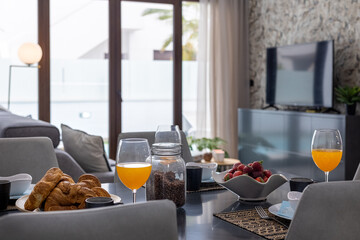 Modern breakfast setup with croissants, strawberries, juice, and coffee beans in stylish living room