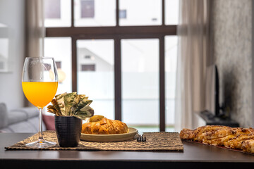 Glass of orange juice with croissants and pastries in modern cozy living room interior