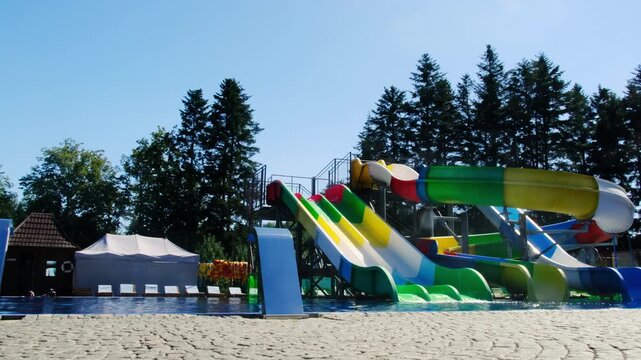 Bright slides and people playing in swimming pool at modern aquapark. Funny attractions to play in water at hotel poolside lit by sunlight