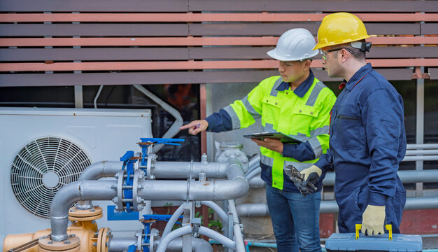 Two professional engineers inspecting industrial air conditioning system outside. Construction workers checking hvac maintenance with clipboard and toolbox at manufacturing factory site plant.