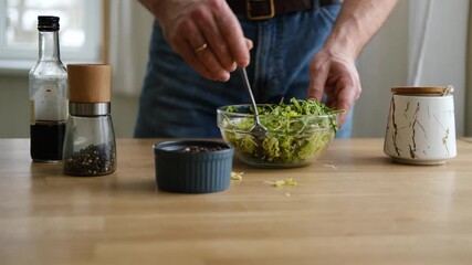 Handsome bearded man is preparing green fresh vegan salad in the kitchen at home. Male cutting vegetables, lettuce with knife on wooden chopping board, cooking vegetarian meal. Tasty healthy diet food - Powered by Adobe