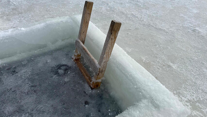 Wooden ladder steps for ice hole swimming in frozen lake surface with thick ice for winter bathing...