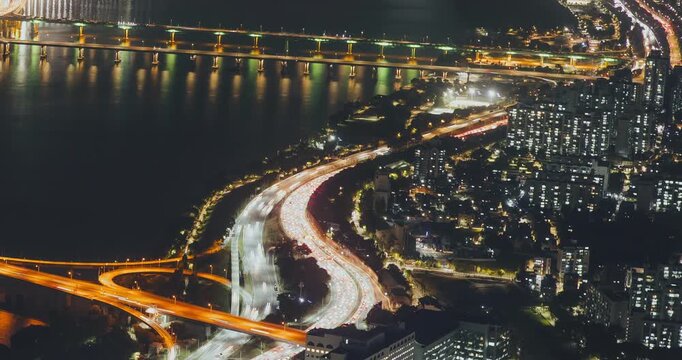 Aerial perspective captures illuminated highways and bridges with flowing traffic, highlighting vibrant city lights and reflections on the water surface. Time-lapse, Seoul, South Korea