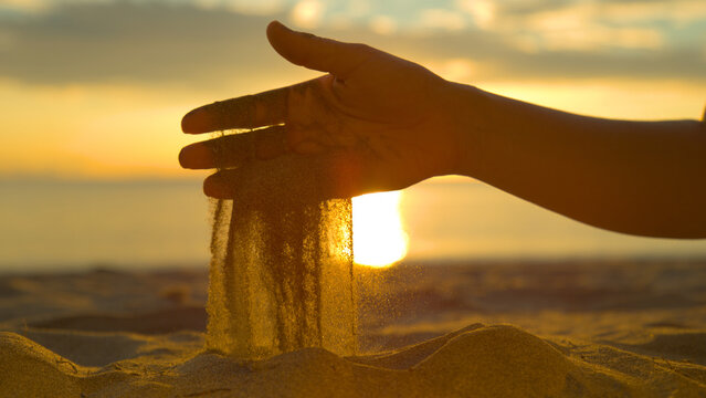 CLOSE UP: Sparkling grains of coarse sand fall out of unknown female's hand.