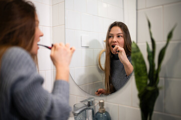 Woman brushing teeth in bathroom mirror reflection