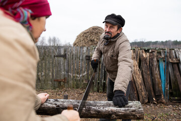 Man and woman cutting firewood with a handsaw. Rural housework