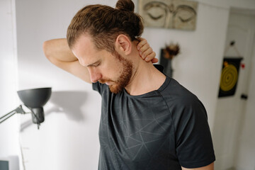 Man stretches neck in indoor space during the day while adjusting posture and feeling tension in muscles