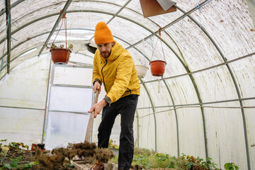 Man digging in greenhouse while wearing yellow jacket and orange hat during gardeners' workday