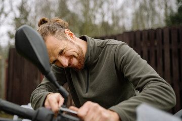 Obraz premium Man straining to tighten rearview mirror bolt on motorcycle using wrench.
