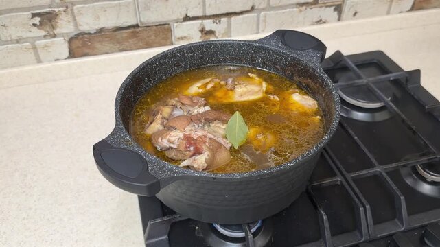 Adding Bay Leaf to Rich Pork Shank and Chicken Broth in Black Pot. Seasoning and Stirring Fatty Meat Soup with Ladle. Traditional Aspic Preparation.