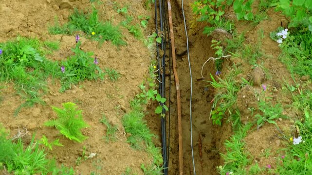Electrical cables placed in narrow trench at countryside upper view. Power supplies underground maintenance in meadow on summer day