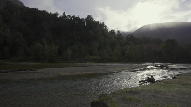 Landscape view of a dense forest bordering the Pichi Traful River at sunrise, with morning light filtering through mist over the mountains