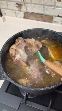 Lifting Tender Pork Shank from Rich Broth and Stirring Fatty Soup with Ladle. Chef Turning Cooked Knuckle in Black Pot for Traditional Aspic or Jelly.