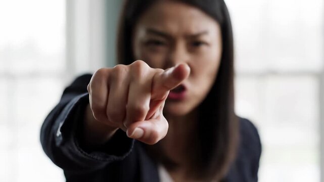 Close-up captures an intensely angry woman pointing directly at the viewer, her blurred face conveying a furious expression. This accusatory gesture symbolizes strong emotional tension and