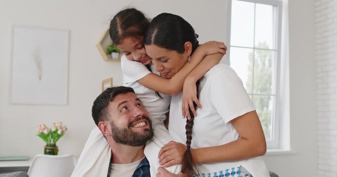 Happy family with daughter laughing at home. Parents embrace as mother lifts the girl while father beams, sharing a smile in a bright room with soft laughter. Concept: happy family at home.