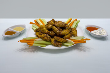 A plate of chicken wings and carrots with various sauces on a table