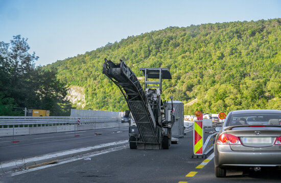 Cold milling machine on a motorway during asphalt pavement removal. The image captures infrastructure maintenance with a car in traffic and green hills in the background: 26.08.2025- Slovenia	
