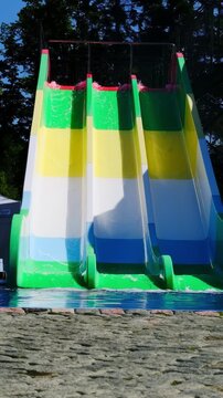 Water flows down multi row colorful water slide against trees. Construction allows visitors to slide smoothly into small pool of water